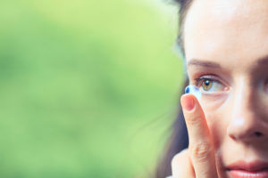 A woman inserts a contact lens in her eye with her finger.