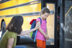 A mother comforts her daughter as she shies away from a school bus.