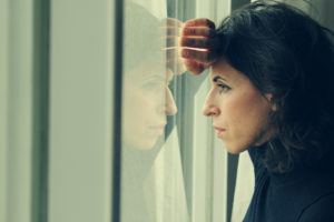 A woman leans her arm and head on a window and looks out. She appears upset.