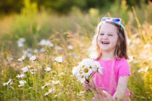 A young girl holds daisies in her hand and smiles big. The girl sits in a field of flowers.