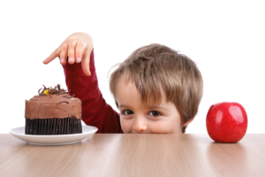 A young boy reaches for a cupcake instead of an apple. He has a mischevious look on his face.