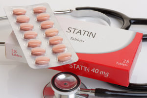 A prescription box reads, "Statin 40 mg tablets." The tablets are shown on top of the box. A stethoscope surrounds the Statin box and tablets.