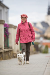 A woman wearing a pink coat and pink hat walks her dog outside.