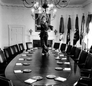 Betty Ford stands on a table and smiles big.