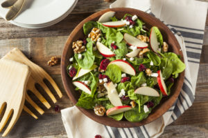 A salad is shown with apples, goat cheese, dried cranberries and walnuts.