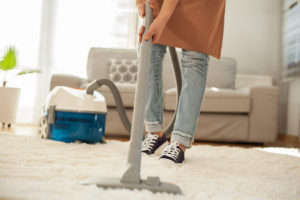 A person uses a steam cleaner on a white rug in their home.