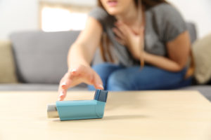 A young woman reaches for her blue asthma inhaler. 