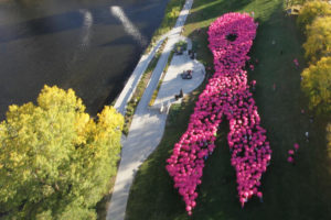 A group of people stand together to form a breast cancer ribbon. They all wear pink T-shirts.