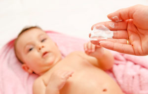 A person holds moisturizer in their hand and appears to be putting it on a baby.