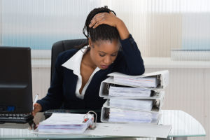 A woman sits at her desk and looks over piles of paperwork.