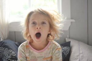 A young girl sits on her bed and yawns.
