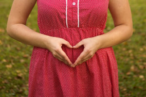 An expectant mother holds her hands over her belly. Her hands are shaped into a heart.