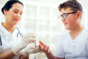 A boy stares at his finger as a medical professional pricks his finger for blood.