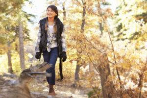 A young woman walks through the woods and smiles.