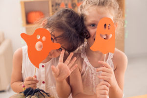 Two little girls hold up two orange ghost-looking signs and smile.