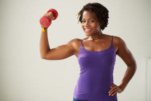 A woman lifts a red dumbbell and smiles.
