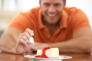 A man places his fork on top of a piece of cheesecake.