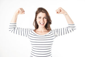 A woman flexes her arm muscles and smiles.