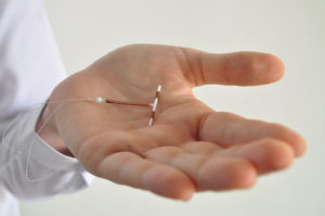 A medical professional holds an IUD in their hand. 
