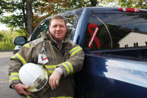 Joe Cooper is shown posing for a photo in front of his truck in his firefighter uniform.