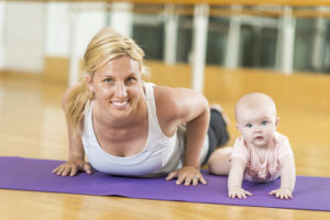 A woman does a push-up next to her baby.