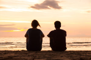 A man and woman stare at the sunset together at the beach.
