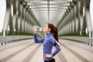 A woman stops running to drink her water bottle.