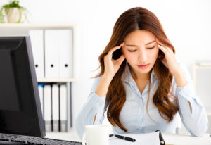 A woman is spacing out at work. She holds her hands to her head and tries to focus.