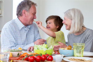 Two adults and a young child are eating vegetables together. 