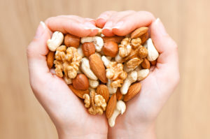 Two hands, shaped as a heart, hold different kinds of nuts.