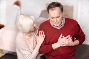 A man holds his hands over his heart and appears to be in pain. A woman tries to comfort him.