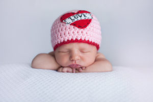 A baby appears asleep wearing a pink hat.