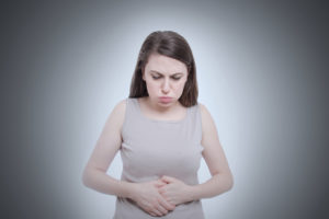 A woman holds her stomach and appears uncomfortable.