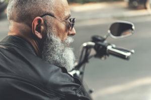 A bearded man with sunglasses sits on a motorcycle. He is not wearing a helmet.