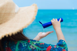 A woman squeezes sunscreen into her hands from a blue bottle.