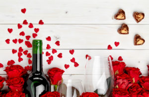 Red roses surround a wine bottole, and two glasses of wine.