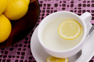 A white tea cup holds hot water and a slice of lemon.