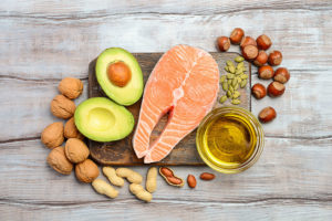Fish, nuts, a healthy oil, and an avacado lie on a cutting board.