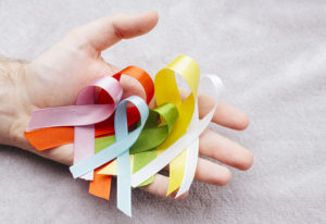 A hand that holds six different kinds of ribbon. Each ribbon represents a different type of cancer.