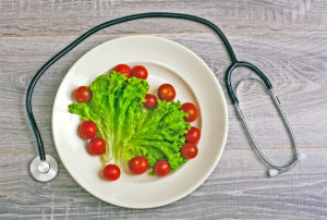 A stethoscope wraps around a white plate with tomatoes and lettuce.