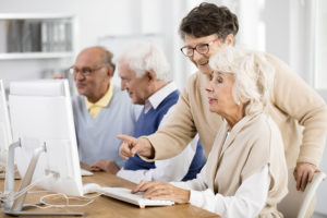 Four elderly adults sit at computers. They all appear to be happy and using the computer.