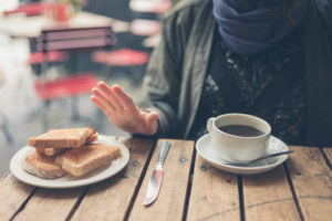 A woman sits at a table with coffee and pushes a plate full of bread away from her.