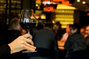 A person holds up a glass of wine at a bar.