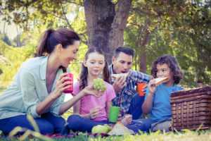 A family sits outside for a picnic. They eat grapes and sandwiches.