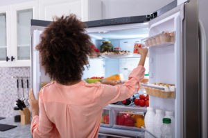 An adult looks inside their fridge for expired food containers.