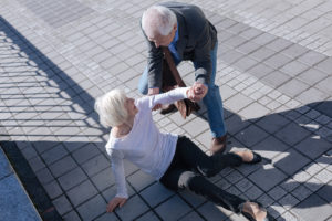 An elderly woman appears to have fallen. A man helps her off the ground.