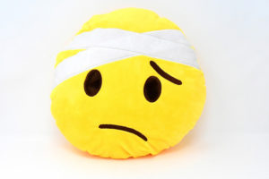 A yellow emoji pillow that appears sick with a bandage over its head.