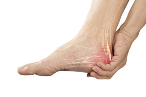 A person holds onto their heel. The heel is colored red to showcase pain.