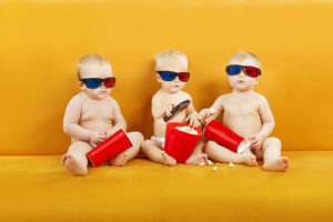 Three babies wear 3-D glasses and hold popcorn.