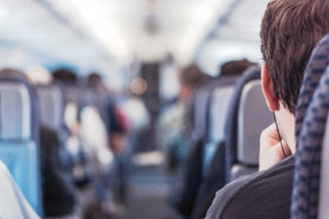 A man wears earbuds on a plane. He appears to be coughing in his seat.